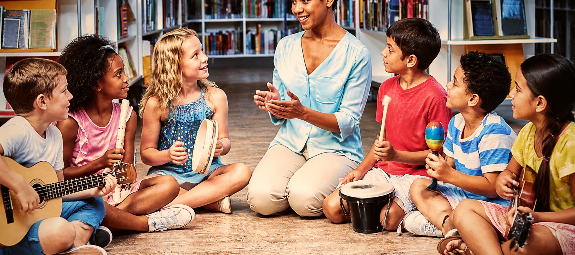 Muziekdocent maakt samen met een groep basisschoolkinderen muziek met tamboerijn, ukelele en trommel